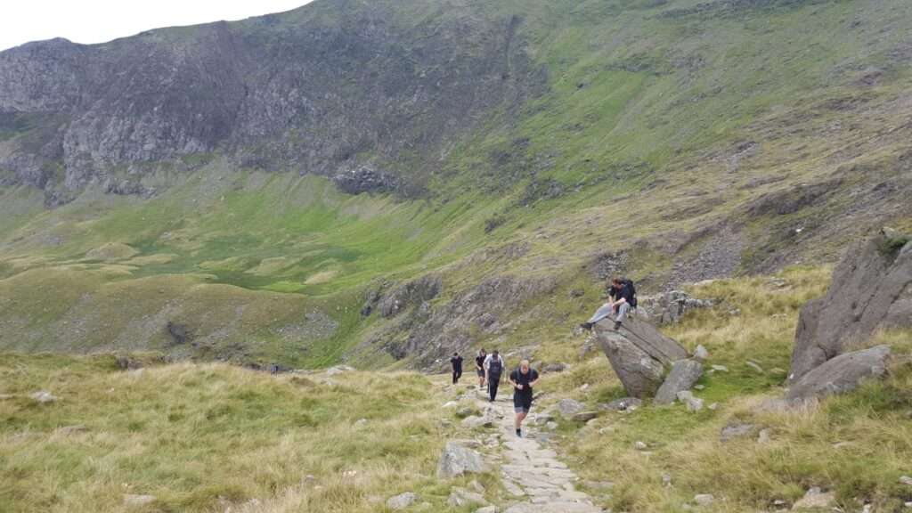 Hikers walking along a scenic mountain trail on Snowdon, Wales, with the peak rising in the background in Snowdonia National Park.