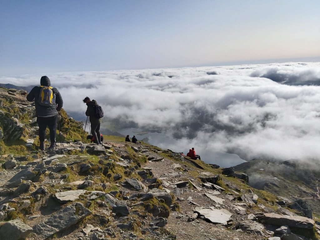 Hikers making their way along a mountain trail on Snowdon, Wales, with the 1,085-metre peak visible in Snowdonia National Park, Gwynedd.
